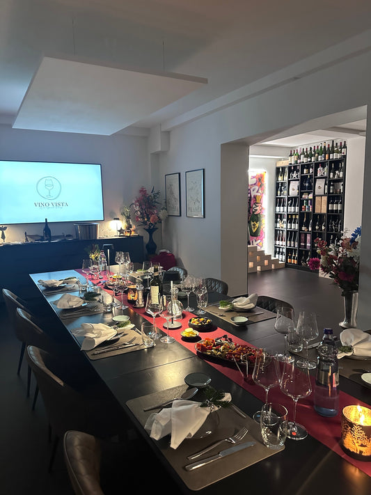 Festlich gedeckte lange Tafel bei Vino Vista mit rotem Tischläufer, Weingläsern, Antipasti und Kerzenlicht