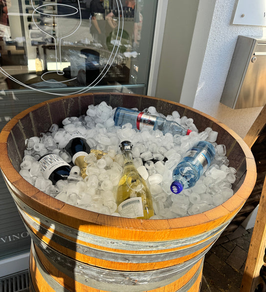 Holzfass voller Eiswürfel mit gekühlten Schaumwein- und Wasserflaschen vor dem Schaufenster der Vino Vista